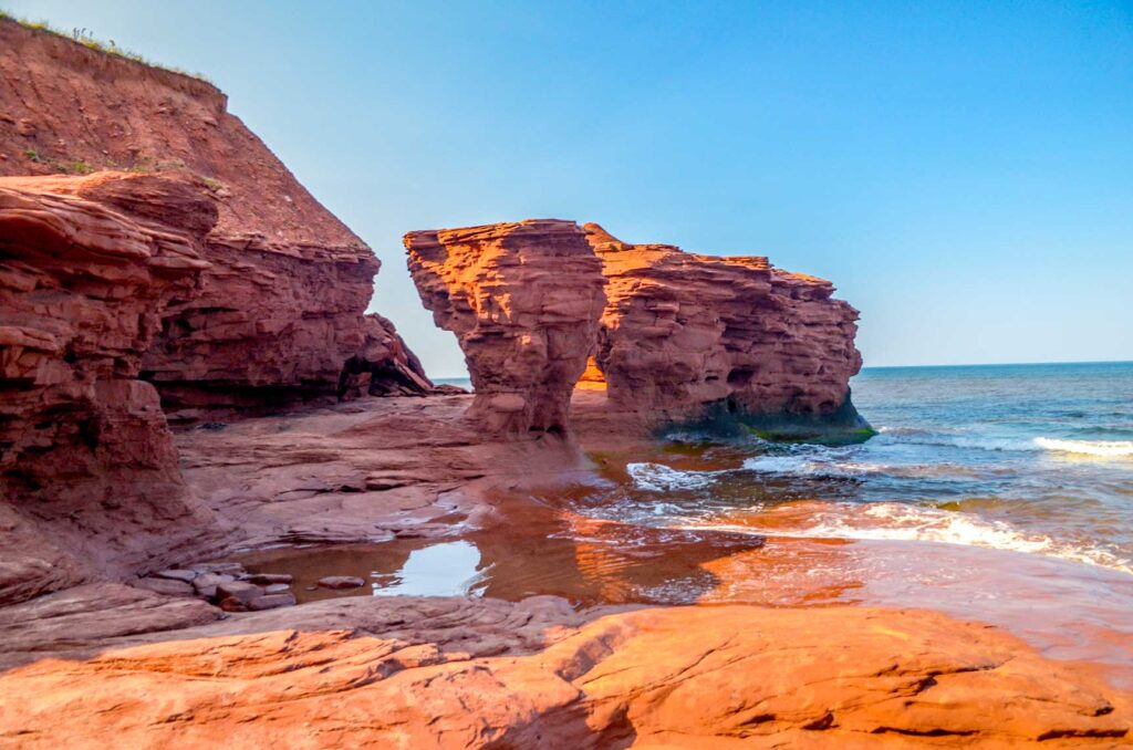 The famous red rocks of Prince edward Island on the shoreline. The rocks are quite edgy with indentations caused by harsh weathers and water hitting the side. The tide is making it's way in, but around this bend used to be the famous teacup rock. 
