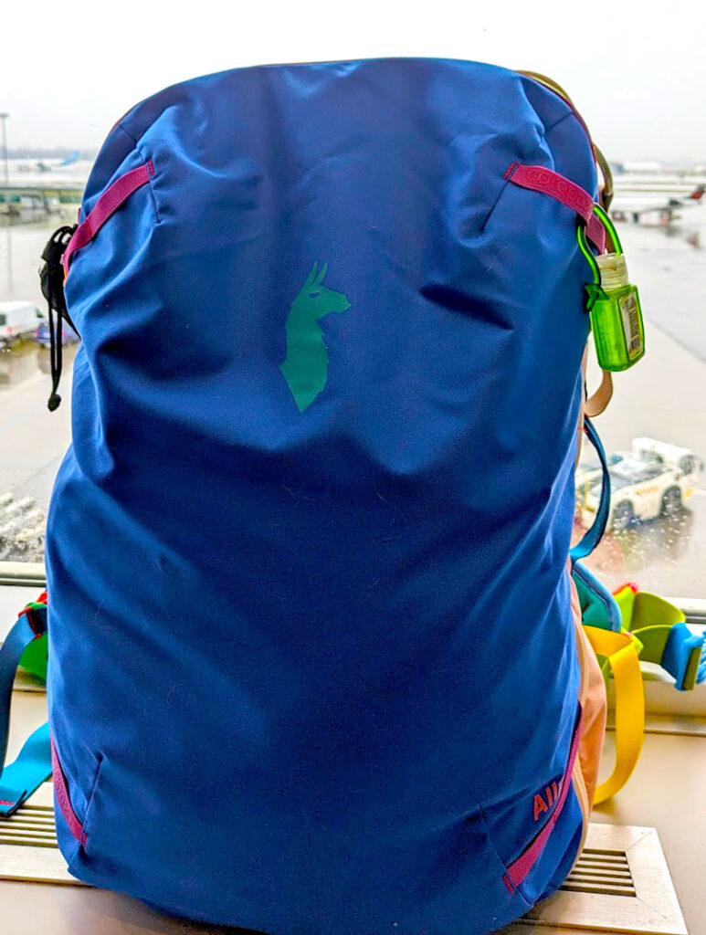 vertical image of a tall vibrant blue cotopaxi allpa 35 Del Dia. There's an outline in a lighter blue of an alpaca in the centre (the cotopaxi logo). A mini purrel is attached to one of the pink loops on the outside of the bag