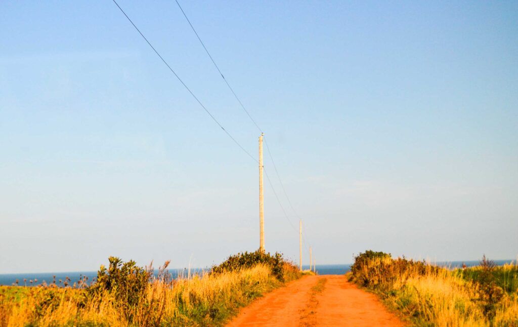 central coastal drive pei off the main roads. Driving on a red dirt road, it looks like off the edge of the world straight into the water below... There are wires connected by poles showing that the road in fact does continue below. The sky is completely clear without one cloud. 