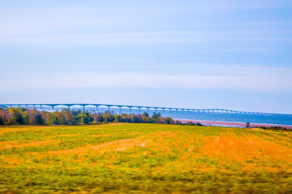 confederation bridge prince edward island going off into the distance of the choppy waters. The red dirt is coming through the grass in front of you on the central coastal drive