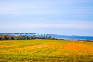 confederation bridge prince edward island going off into the distance of the choppy waters. The red dirt is coming through the grass in front of you on the central coastal drive