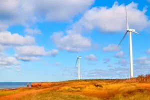 wind energy on the tip of the north cape coastal drive prince edward island. Giant white wind turbines are located all along the coast way into the distance. The red land ends adn the sea begins