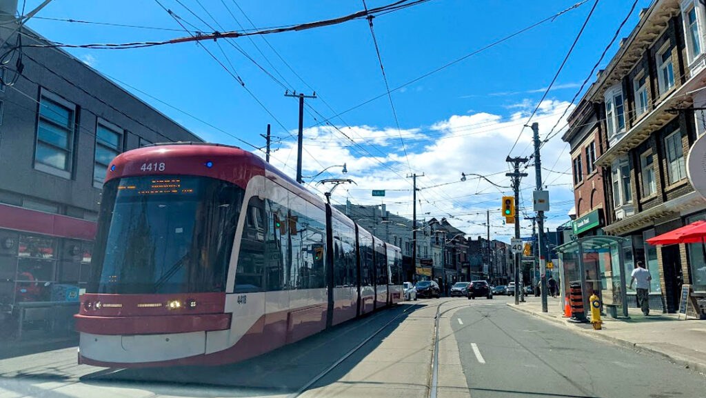 the streets of toronto with a red and white street car coming your way in the middle of the road. 