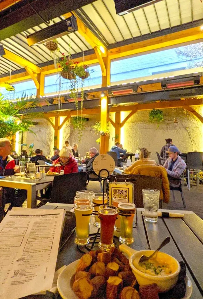 a vertical photo inside Druthers brewery with a pub snack, the menu for ordering more, and a flight of six beers to share among two people.