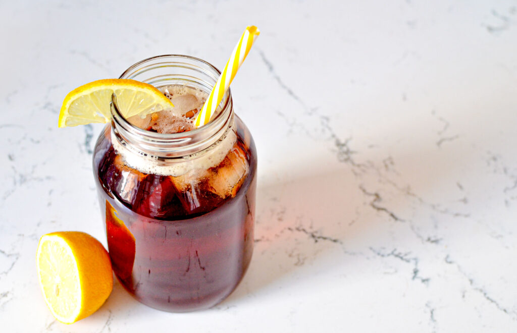 ice-tea-in-mason-jar on a marbled counter top with a lemon wedge on the side and slice on the rim of the glass. There's even a yellow striped straw to match!