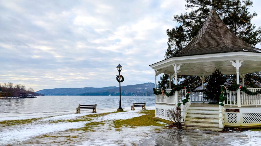 a gazebo in a park near the lake in North Hatley Quebec in the eastern townships. The snow is melting so you can see the grass. Across the lake are the silhouette of the mountains