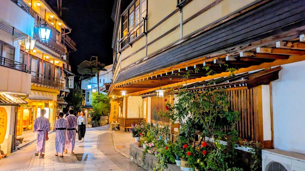 shibu onsen japan at night: traditional japanese buildings line a narrow stone street. people in traditional bathrobes (yukata) are walking to public baths in japan