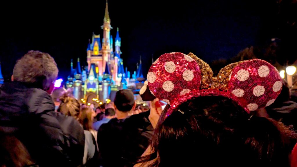 disney-castle-lit-up-at-night-with-a-crowd-in-front-of-it-and-a-woman-with-long-hair-with-mickey-ears-bought-from-amazon