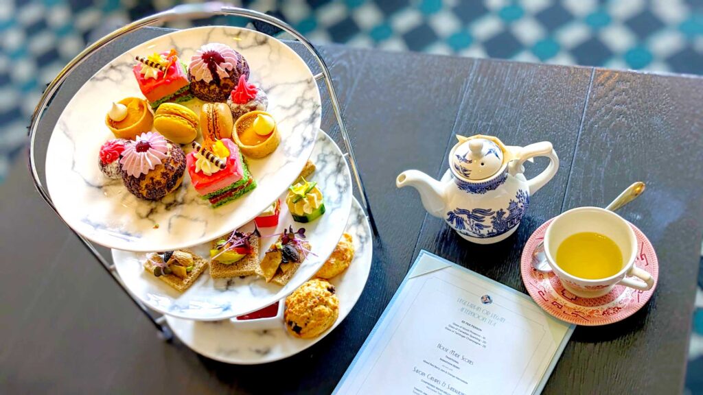 top down view of a three tiered afternoon tea plate. You see all ten desserts on the top plate. On the table is also a teacup filled with tea and a teapot. Theres also the fairmont afternoon tea menu