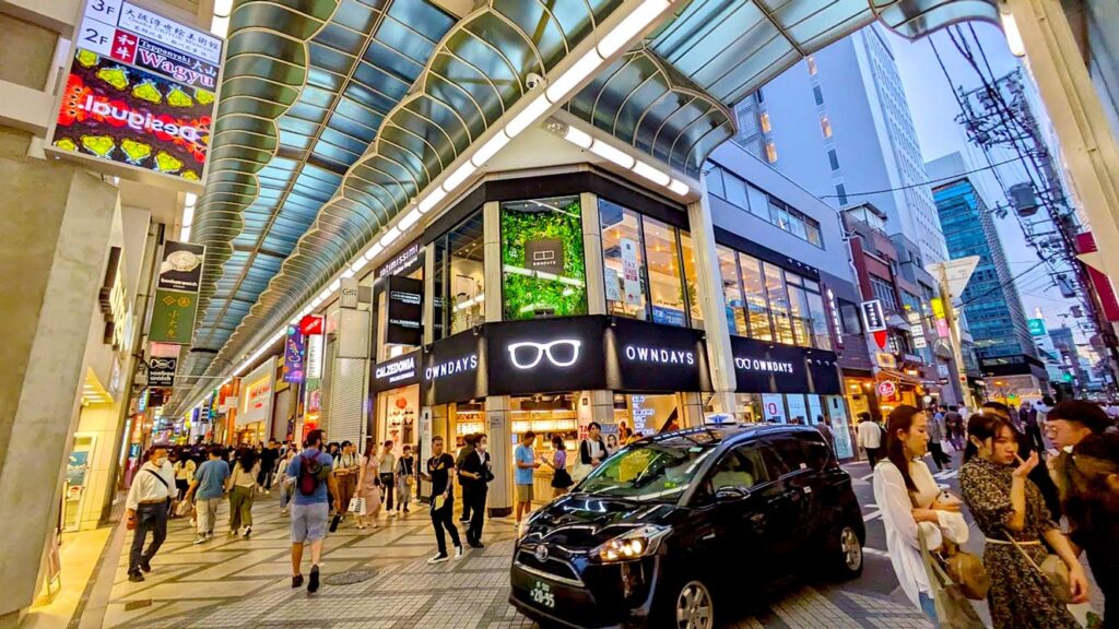 an example of a japanese shopping mall in osaka. The mall is half open. Theres a roof very high above. And there are shops on two levels on either side of the street. But cutting the mall in half is a car driving through on the road, and you notice that half the mall is actually outside. 