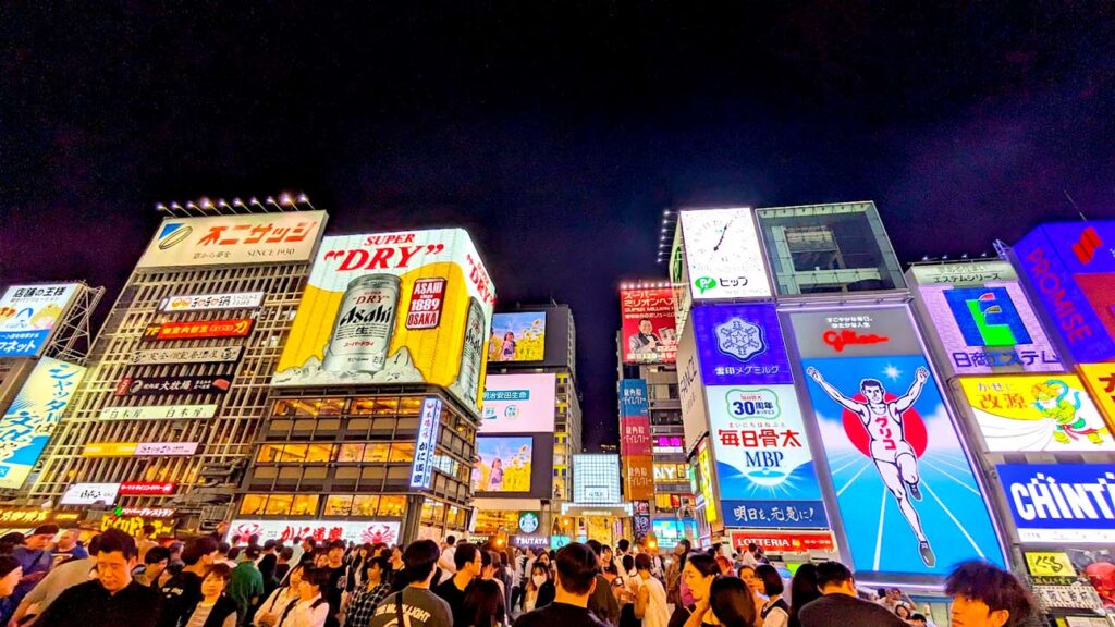 osaka dotonbori area at night. Its packed with people, you can't even see between everyone its so packed. above everyone are the giant lit up signs including the glico sign with a man running