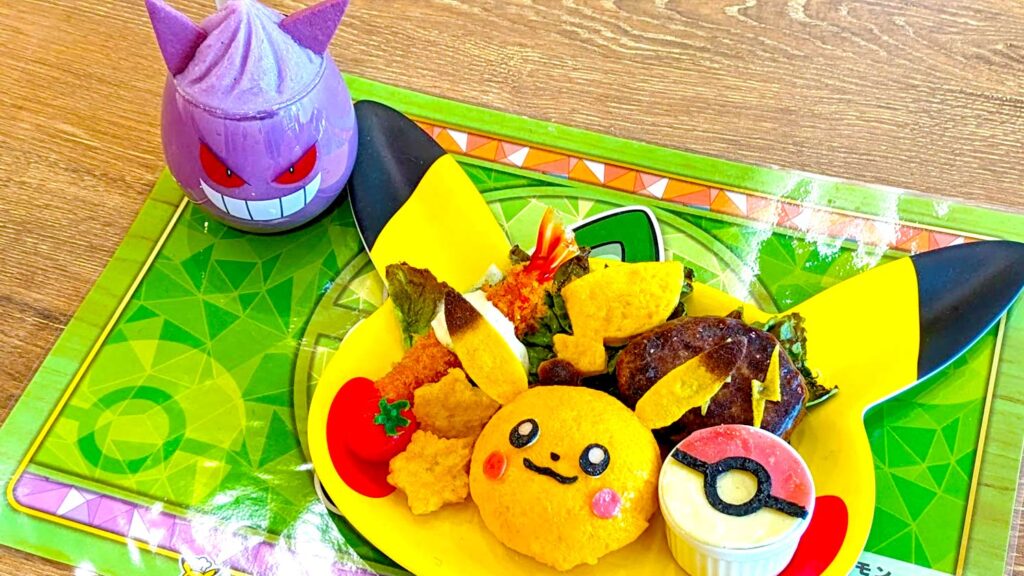 a meal served at the pokemon cafe. Its served on a pikachu shaped plate, with a pokeball side dish, yellow coloured rice shaped into pikachus face and tail. On the side is a gangar glass filled with purple slush drink