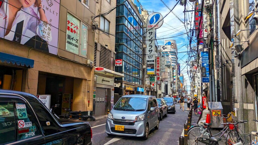 a side street in osaka japan. the cars are backed up on way. wires line the skyline view crossing the street to reach all the buildings