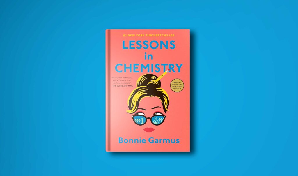 hardcover book on a plane blue background to compliment the orange book cover of lessons in chemistry by Bonnie Garmus