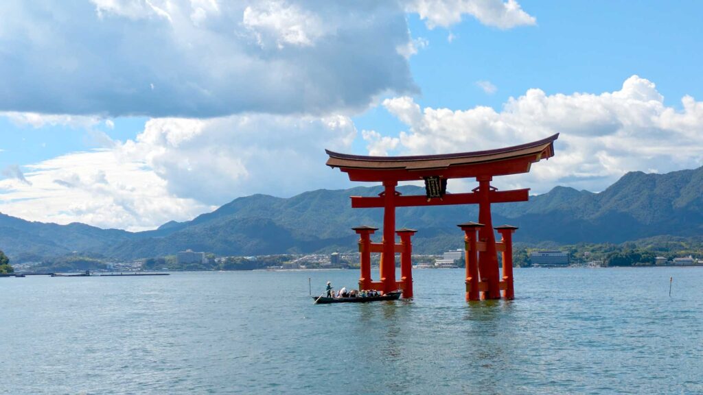 the otorii gate during high tide. The pillars are mostly covered by water now, and there's a long, old school boat that is about to float through the famous floating gates. 