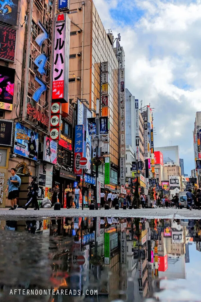 the streets of tokyo in shinjuku , it's bustling  after it rained, there's a reflection of the streets in the puddles
