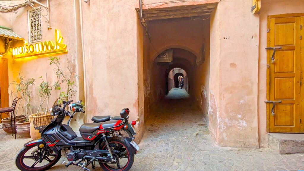 an unassuming dark alley off that's easy to miss of a main street. It's like a tunnel, with a rounded roof above it, and not a lot of light. It's next to a closed wooden door, an what looks like a fancy restaurant with a motorcycle parked outside