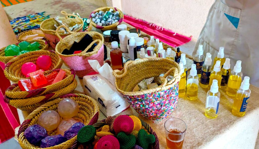 a sneak attack photo of a moroccan argan oil sales pitch. There's a table, where you see the bottom of an apron of someone standing behind it. The table is filled with all the argan oil products for sale, mostly in small spritz bottles, varying degrees of fullness as they gives these out as samples to try on your persons. 