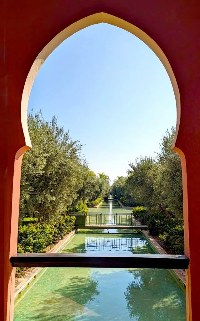 a view through the beautiful Moroccan arched open window frame at the club med Marrakech looking onto the gardens with a stream of water flowing through lush olive trees