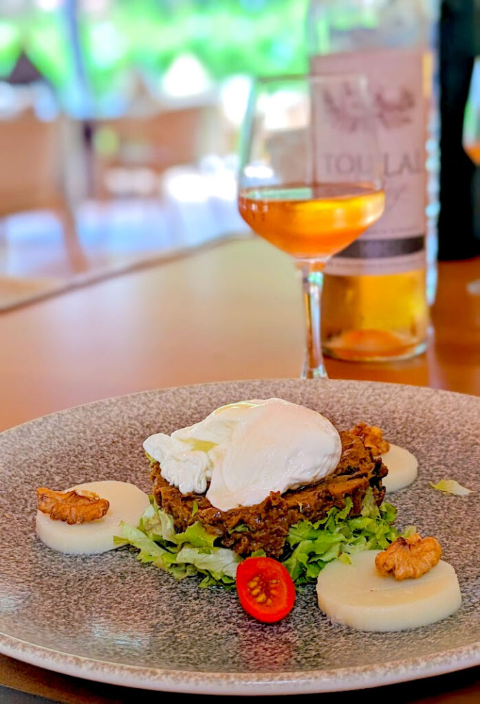 appetizer at el kebir at the club med la palmeraie in marrakech morocco. A plate mostly empty, but there are some slices of hearts of palm, with walnuts on top, and tomatoes in between. An eggplant pate rests on top of green lettuce. On top of the eggplant is a poached egg. Behind the plate is a glass and bottle of rose wine