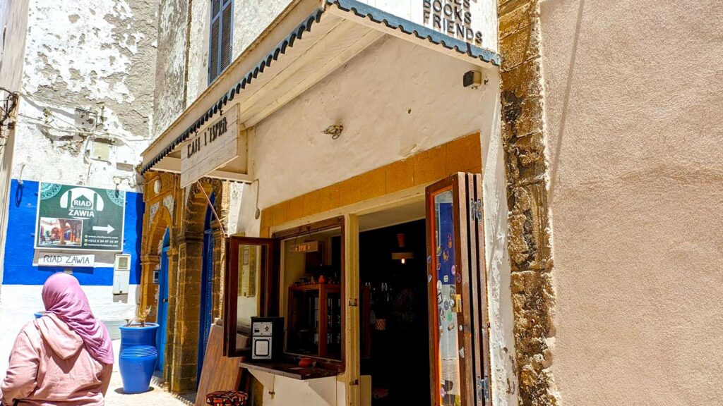 a woman walks by a cafe wearing a full head wrap that also covers her neck