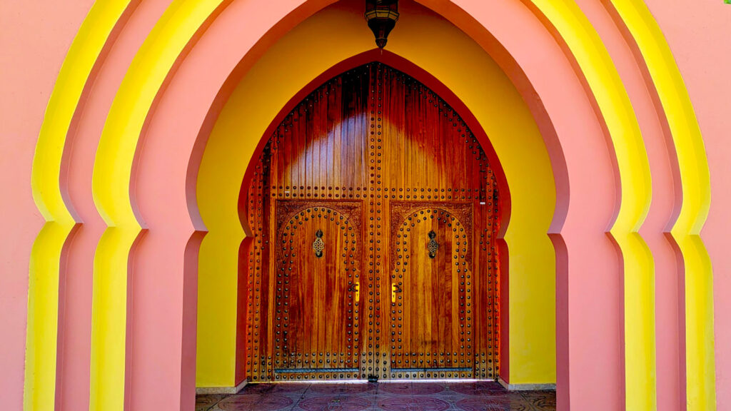 an over the top Moroccan style doorway. Thereare 4 arched doorframes, alternating pink and yellow paint and each a bit more indented than the last one until finally reach reach a much smaller wooden door in the same arched shaped as the doorways.  