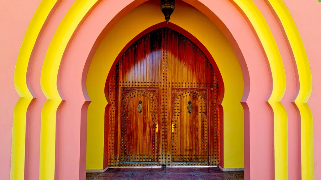 an over the top Moroccan style doorway. Thereare 4 arched doorframes, alternating pink and yellow paint and each a bit more indented than the last one until finally reach reach a much smaller wooden door in the same arched shaped as the doorways.  