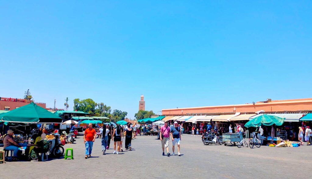 the jemaa el-fnaa square, facing the koutoubia, you can only see the tower peaking out from behind some trees in front of it. The market isn't as busy as it could be, with open space in the centre but there are still some pop up shops on set up with green tents and umbrellas on the sides. There are also some awnings connecting to the building with their souvenirs for sale outside on the sidewalk