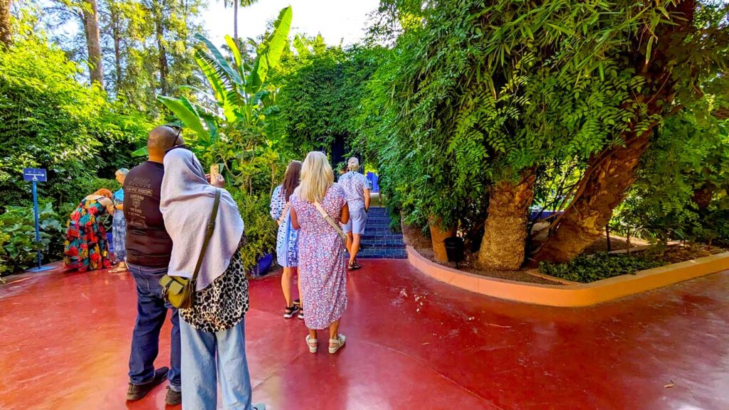 the line up at the jardin marjorelle starts 40 minutes after opening. There are three groups waiting in a line to walk up some stairs into a leaf covered veranda 