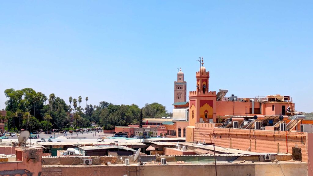 two orange red mosques rising above all the other rooftops in Marrakech, they're even taller than the green trees below them. You can see speakers attached to the top of the closer one