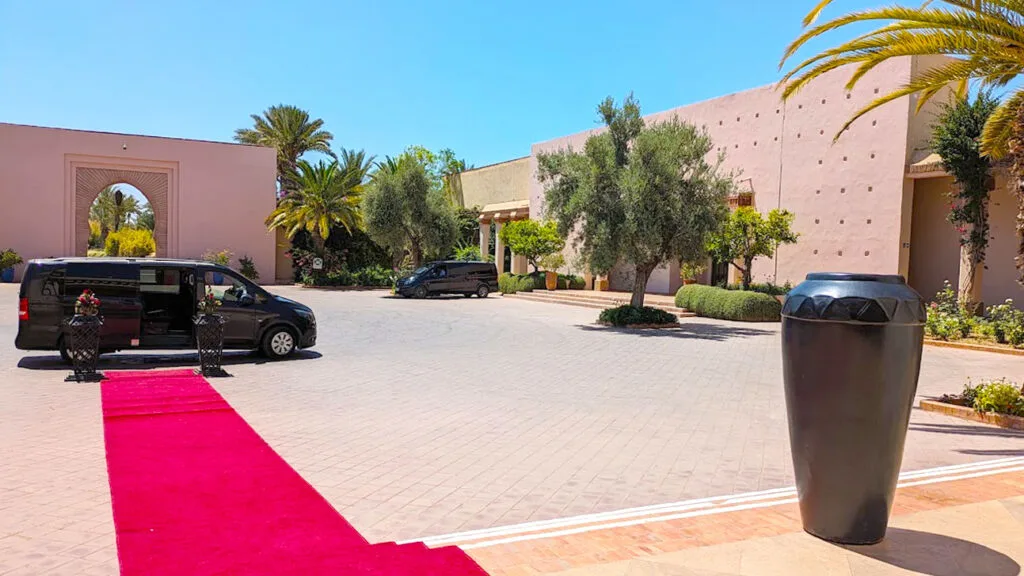 a red carpet leads down from a few stairs all the way out to a black van in a courtyard at the club med in marrakech