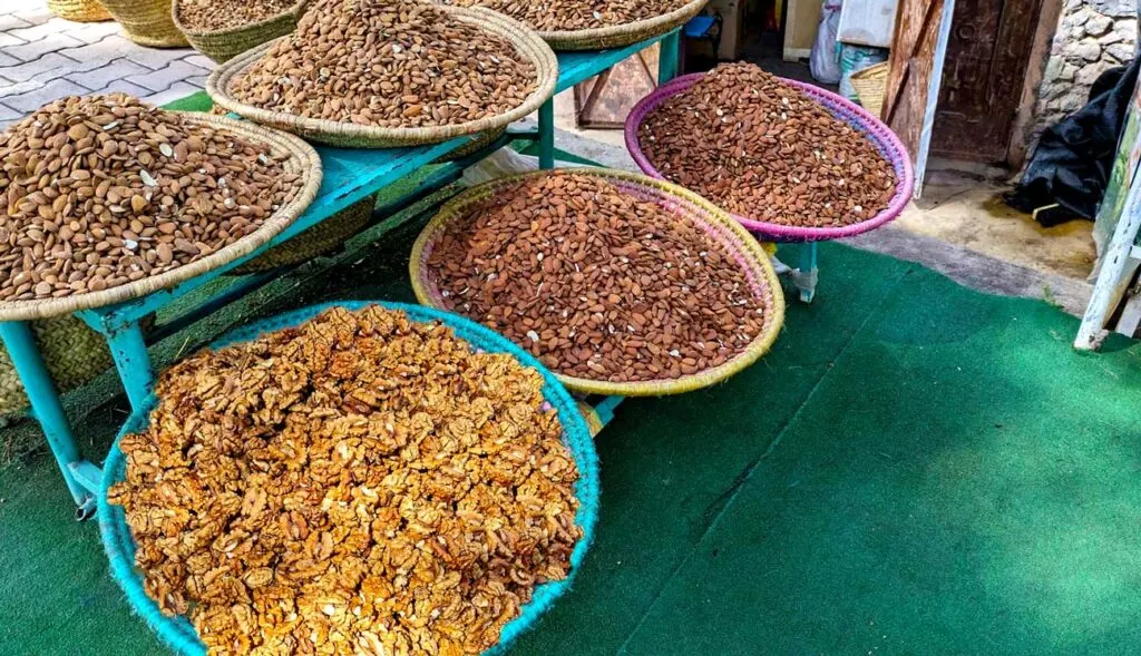 outside of a shop is a two level bench with straw wide baskets, each are filled with walnuts or almonds