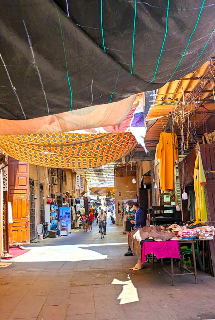 marrakech street that is covered with patterned sheets. People are walking in the distance. 