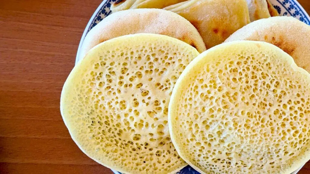 Semelina-(Behghir) moroccan foods to try a typical breakfast. A plate is filled with traditional moroccan breads. The one on top is Semelina (Behghir). It looks like a traditional pancake but with a lot of tiny holes