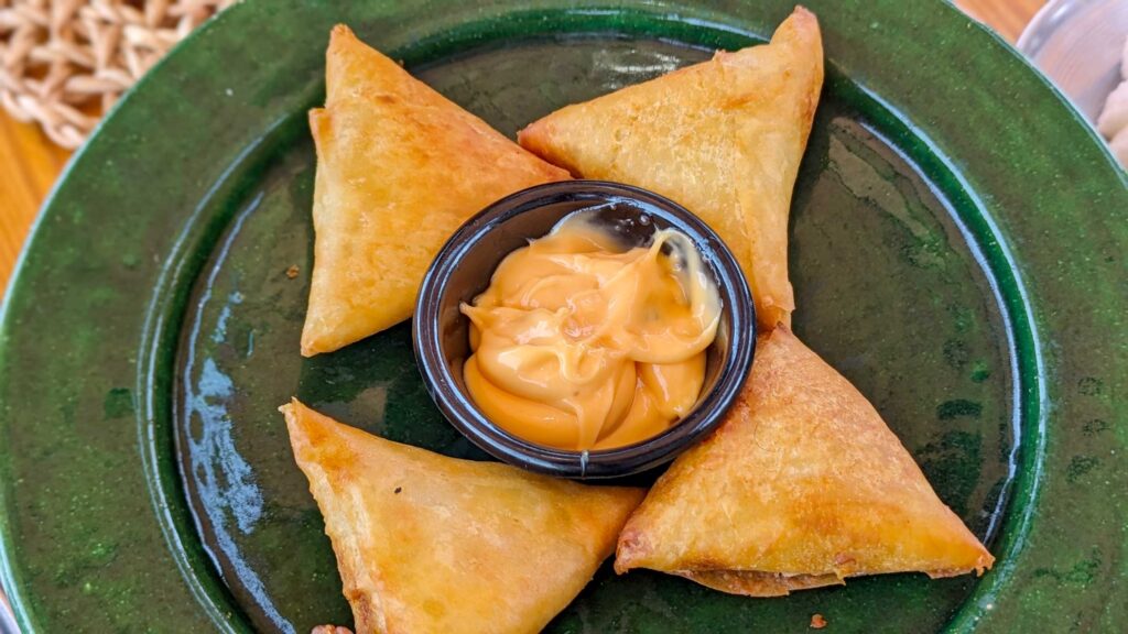 Four Briouat on an ever green plate with a black  ceramic cup in the middle filled with spicy mayo. The Briouat are four fried dough triangles  