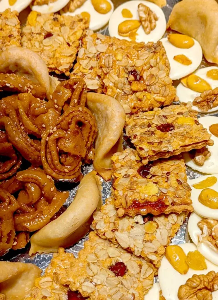 a display of a selection of moroccan desserts. In the middle is chebakia - a rose shaped dessert, encircling those are gazelle horns, then there are square crackers, a circle cracker and more gazelle horns around the edge