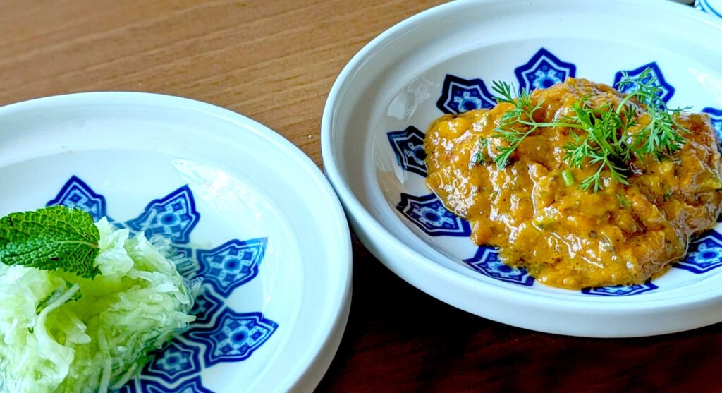 two plates with a blue flower in the middle of each with a salad in the middle of the blue flower. On the left is a cucumber strip salad, and on the right is zaalouk. An eggplant spread