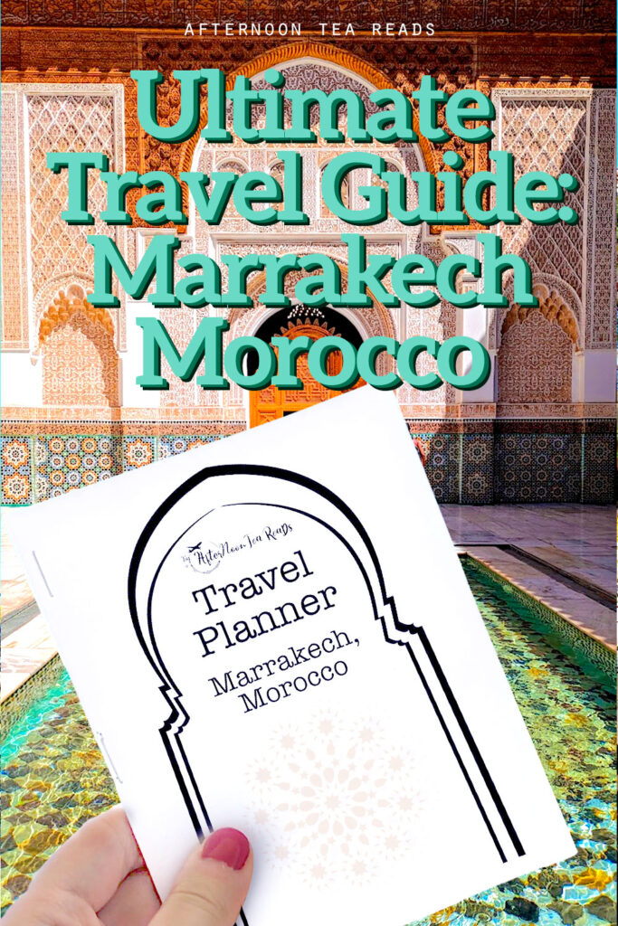 vertical image with text on top: ultimate travel guide: Marrakech Morocco. Underneath is a hand holding up a 4.25 x 5.5 size pocket travel planner. You can see the cover page which has the silhouette of a Moroccan crescent moon doorway. In the background is traditional moroccan architecture in reddish, sand, and light pink hues. 