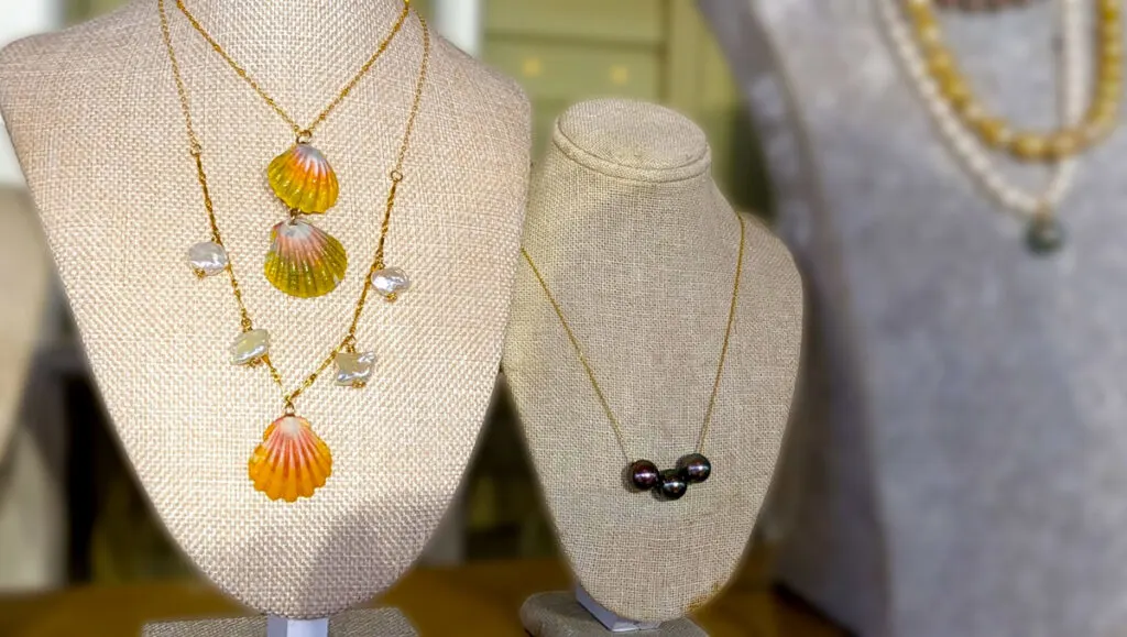 a mannequin bust showcasing three necklaces, with imperfect pearls,  and sunrise pearl pendant. The sunrise pearl goes from green purple to golden yellow