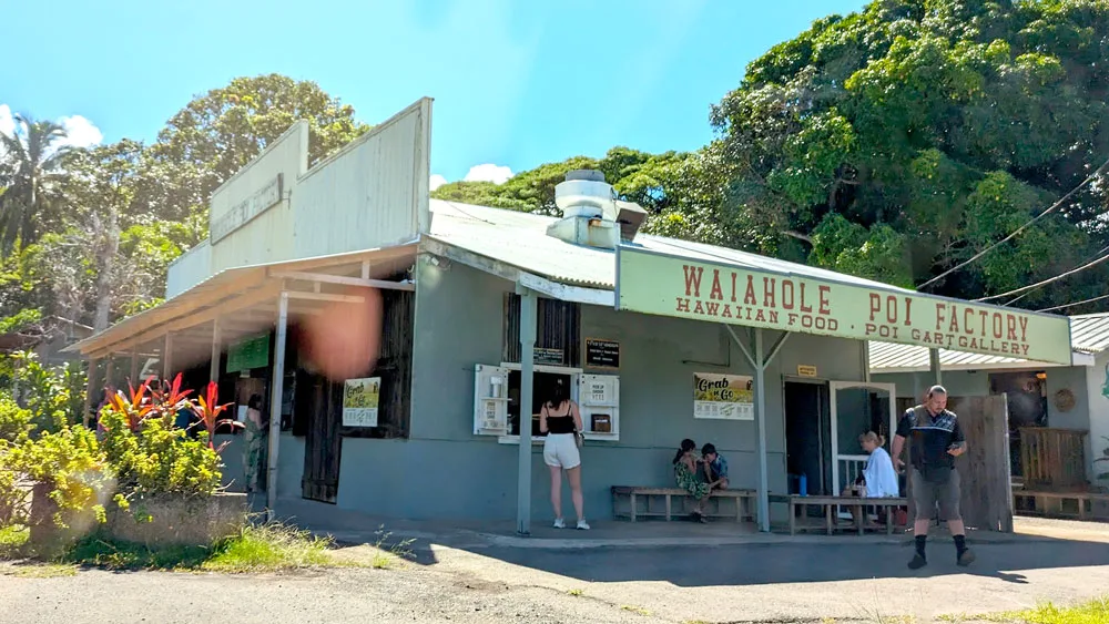 the outside of the waihole poi factory. People are standing at the open windows outside putting in their orders. 