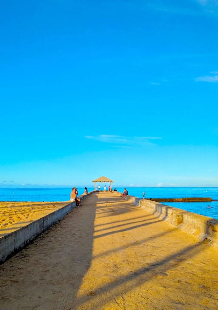 a simple image separated into two parts be the ocean. Above the ocean is completely clear blue skies. Below is a small gazebo at the end of a sand covered path.