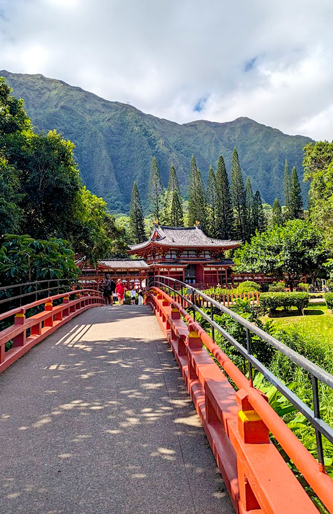 a beautiful relaxing scene that makes you unsure of where you are. A red painted rounded bridge leads you across a stream to a Japanese temple of the same colour. It seems so small compared to the towering deep green mountain behind it. Are you in Japan or Hawaii here - that is the question. 