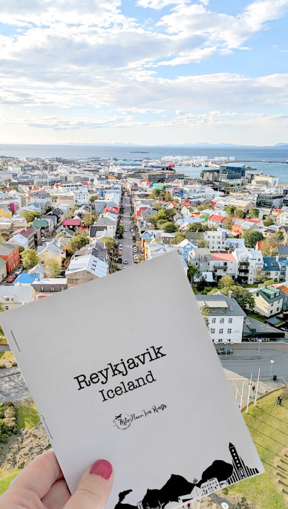 a vertical image of the colourful streets of reykjavik from above. A hand his holding up a small travel booklet for reykjavik Iceland 