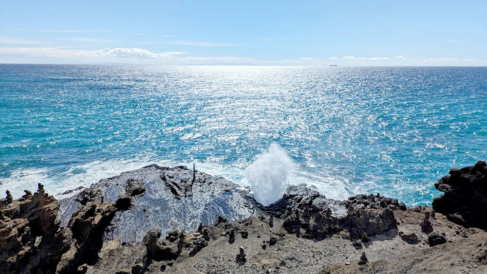 the image is divided into three horizontal sections. On the bottom is black lava rocks on the shore end. Then you have the vast ocean hitting the rocks and leading all the way into the sky. But something stands out between the water and the rocks - a spray of water that came out of the halona blowhole. 