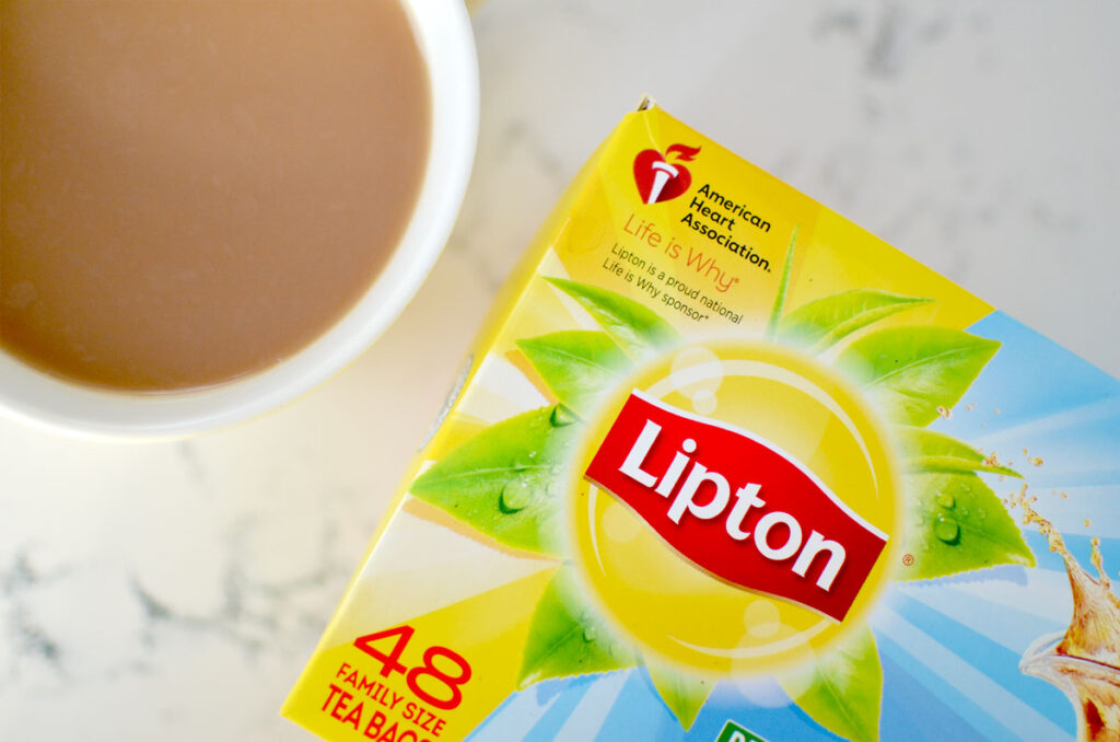 a top down view of a mug with a milk brown brew and a tea box on the counter. The tea box is for Lipton tea, it's a yellow green and blue box. 