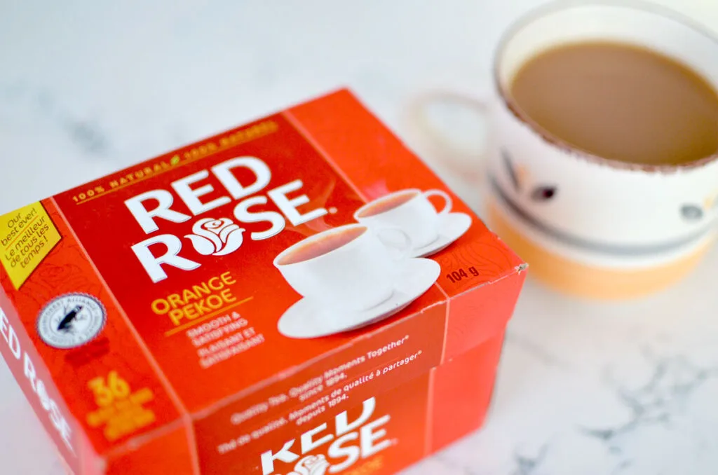 A photo showcasing the red Red Rose Tea box with a steeped mug with red rose tea on the side, slightly out of focus.