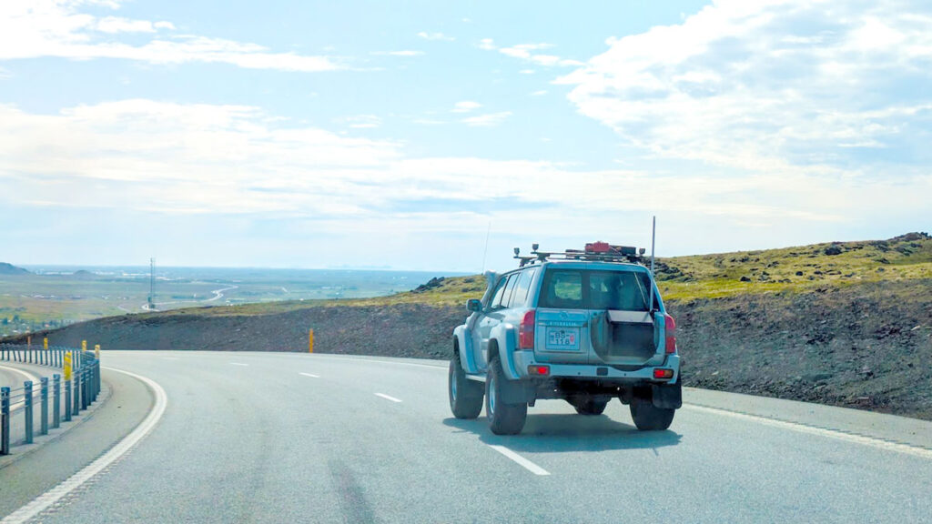 a super jeep driving down a curved Iceland's ring road going downhill towards the valley below. It's a clear day with blue skies and a bit of clouds.