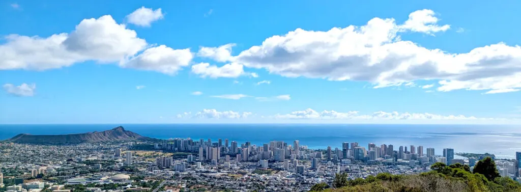 a panoramic image from tantalus lookout. On the left is diamond head, it leads all the way to a lot of tall buildings in the centre, the land ends and the ocean begins and leads your eye right to the horizon where it meets the sky. 