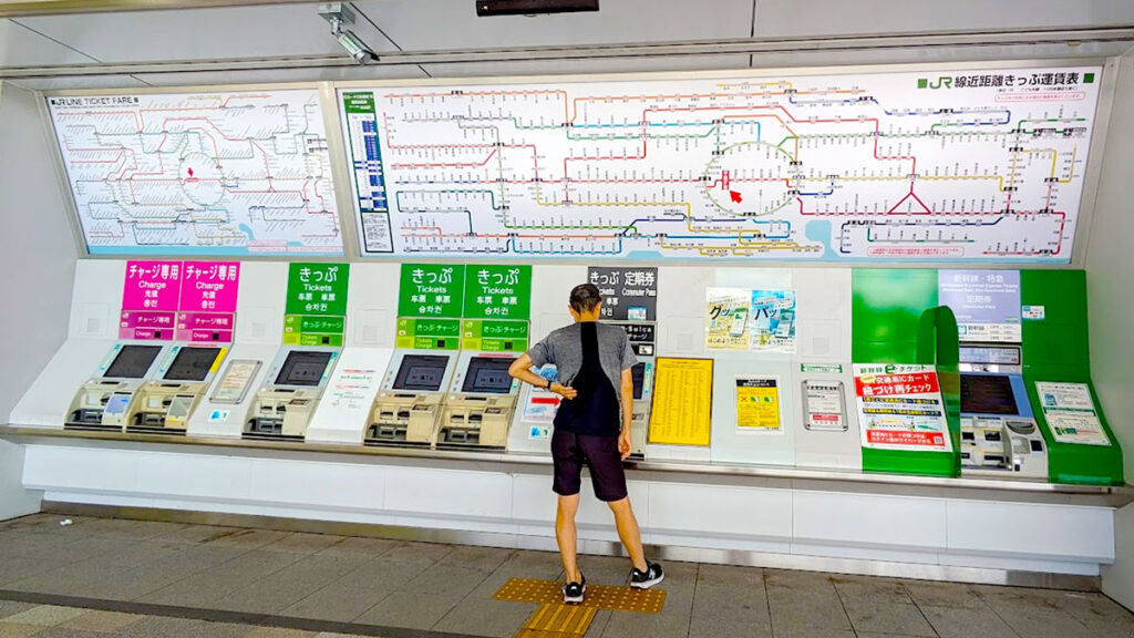 a lone man stands with his back to the camera, looking down at a screen, possibly buying a pass for the train. There's a HUGE map above his head showing the train lines and connections. It can be quite overwhelming because it's so large