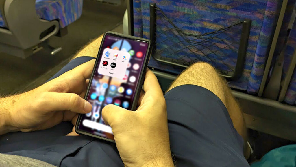 a man sitting on his phone but you can see the screen. The background is blurred except for a group on the home screen. It shoes all the necessary traveling apps for only knowing English in Japan: Google Transale, Airalo, Lens, Uber, and it also shows the Air Canada app